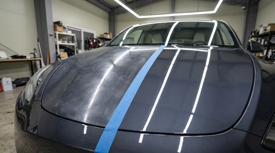 Paint correction 50/50 on a grey Tesla hood: swirls on one side of the tape, mirror finish on the other